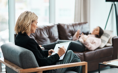 Shot of a mature psychologist writing notes during a therapeutic session with her patient